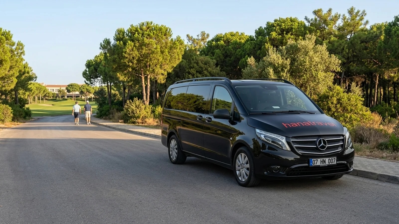 A black transfer van stands on a flat asphalt road framed by pine trees near Belek.